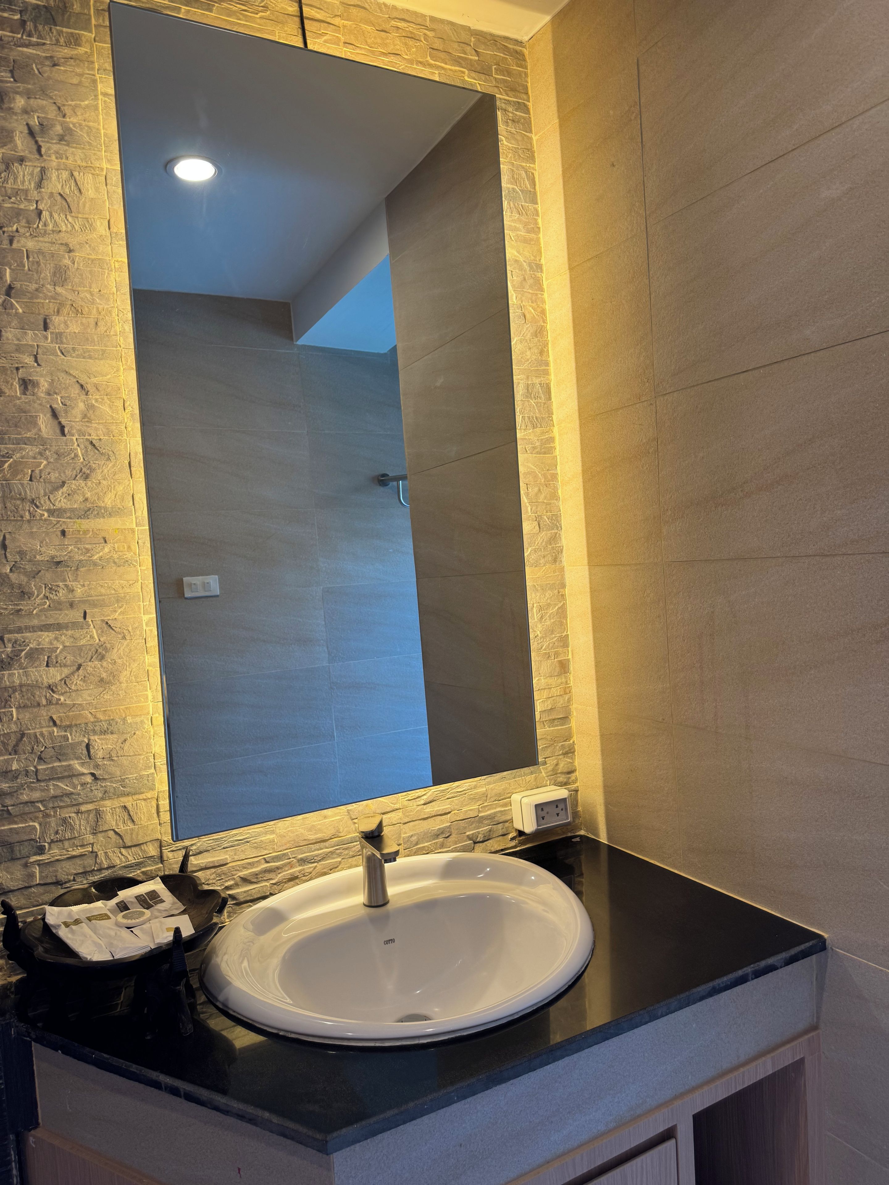 A bathroom with a white sink, a mirror, and a stone-textured wall.