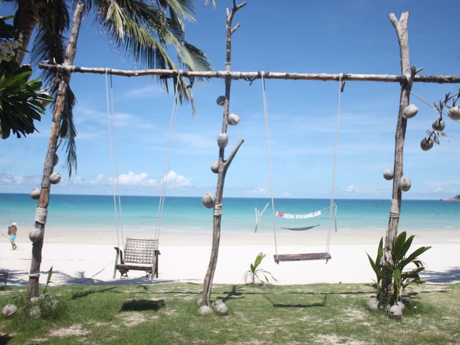 Una playa con un columpio, una hamaca y un banco.