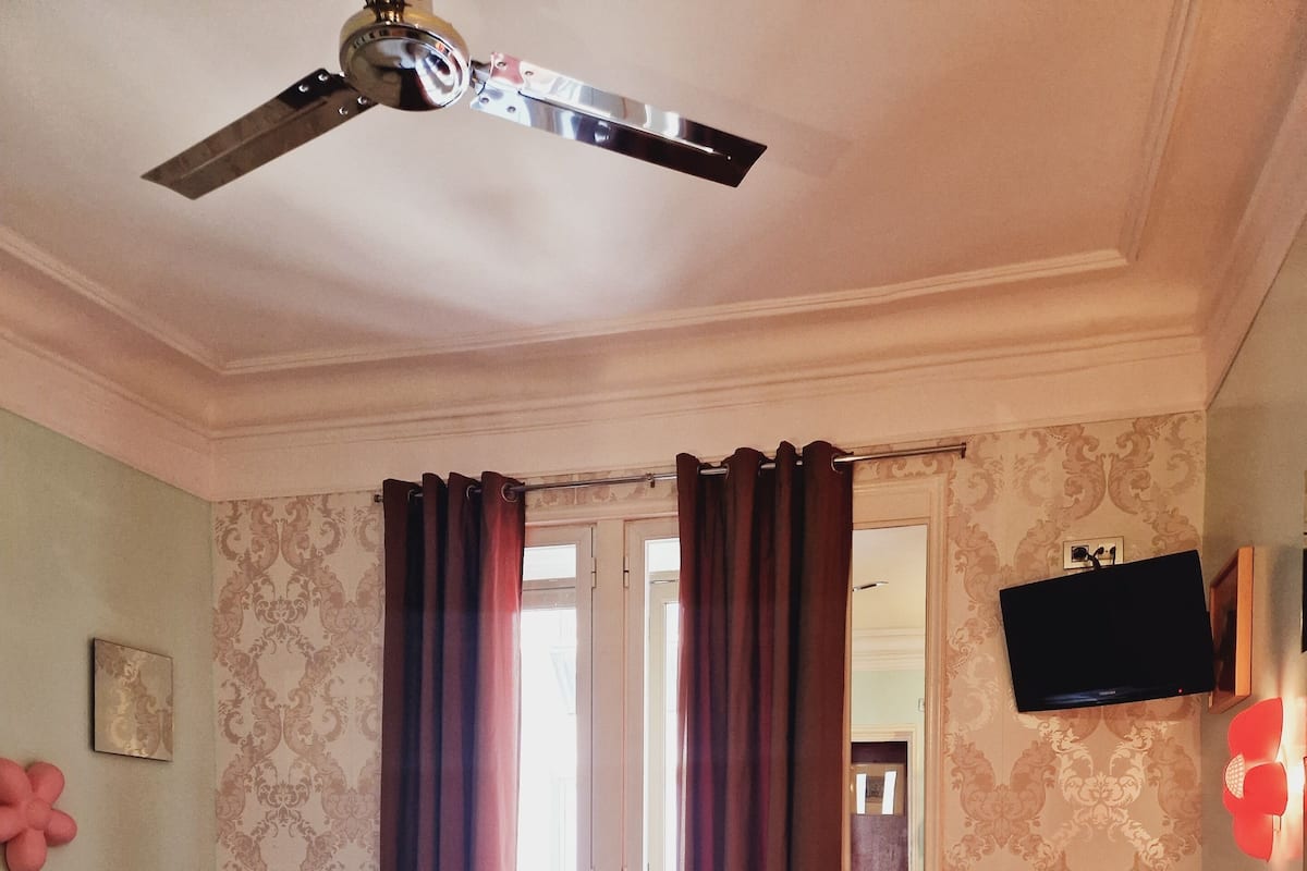 A hotel room with two beds, a ceiling fan, a TV, and a view of the outside.