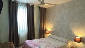 A hotel room with a bed, a nightstand with lamps, a wooden table, a bathroom with a sink and toilet, and a ceiling fan. - Hostal Dolcevita (Madrid)