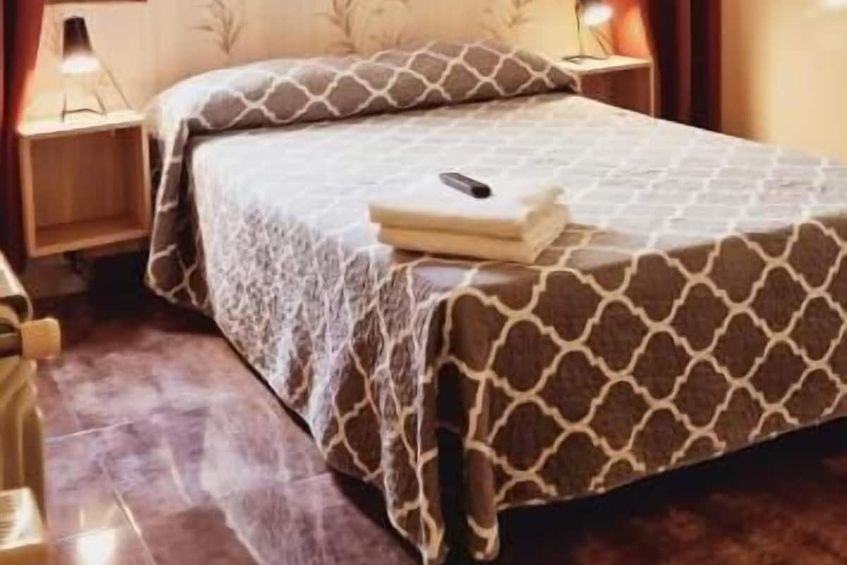 A bedroom with a bed, a ceiling fan, a nightstand, a lamp, and a window with curtains.