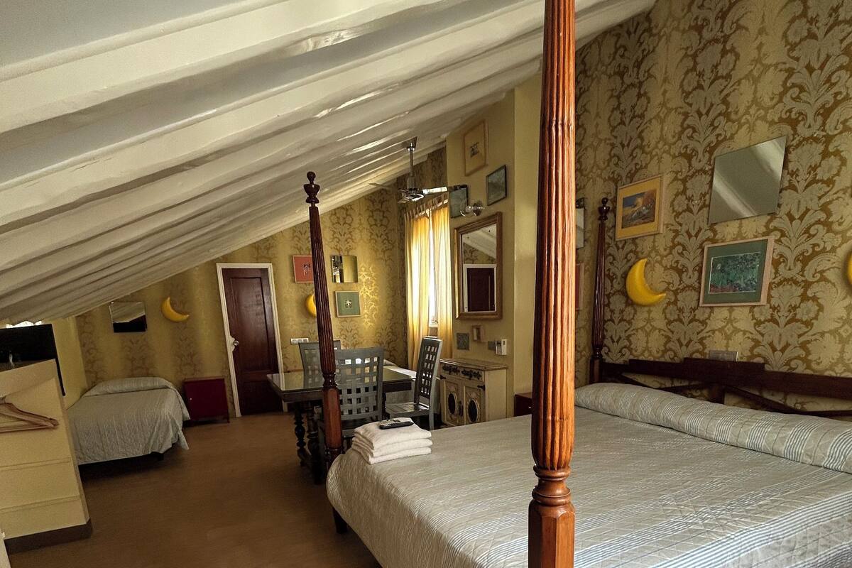 A bedroom with a four-poster bed, a separate sitting area with a table and chairs, and a small desk with a chair.