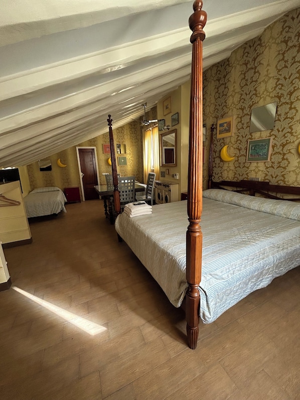 Un dormitorio con cama con dosel, un área de estar separada con una mesa y sillas, y un escritorio pequeño con una silla.