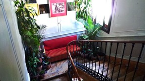 A staircase with a wooden railing leading to a red cushioned bench area. There are multiple potted plants around the bench, and a framed picture is visible on the wall. - Hostal Dolcevita (Madrid)