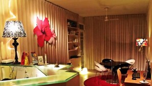 A hotel room with a glass partition, a desk with a chair, a red rug, a television, and a large flower decoration on the wall. - Hostal Dolcevita (Madrid)