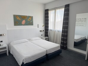 A hotel room with a double bed, a bedside table, a nightstand, a wall-mounted artwork, a window with curtains, and a mirror. - B&B HOTEL Milano Cologno Sporting (Cologno Monzese)