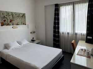 A hotel room with a bed, bedside table, a desk with a chair, a mirror, and a window with curtains. - B&B HOTEL Milano Cologno Sporting (Cologno Monzese)