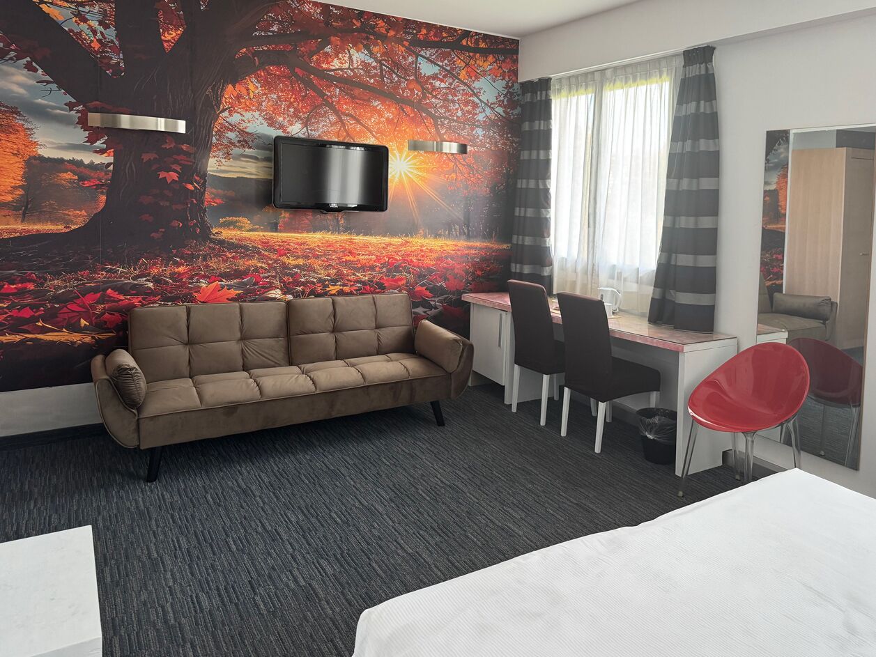 Ein Hotelzimmer mit einer Couch, einem Schreibtisch, einem Sessel, einem Fernseher und einem großen Wandbild.