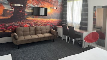 Ein Hotelzimmer mit einer Couch, einem Schreibtisch, einem Sessel, einem Fernseher und einem großen Wandbild.
