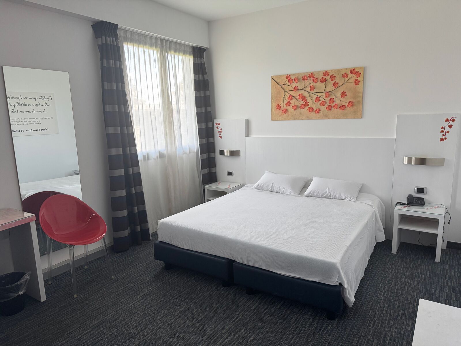 Habitación de hotel con cama, escritorio, silla, mesita de noche y una obra de arte en la pared.