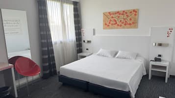 Habitación de hotel con cama, escritorio, silla, mesita de noche y una obra de arte en la pared.