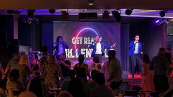 Un escenario con una pantalla grande que muestra los textos 'GET REAL' y 'KILL IT', rodeado por un público en un local con poca luz.