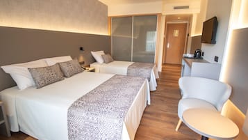 Habitación de hotel con dos camas, zona de estar, escritorio y televisor.