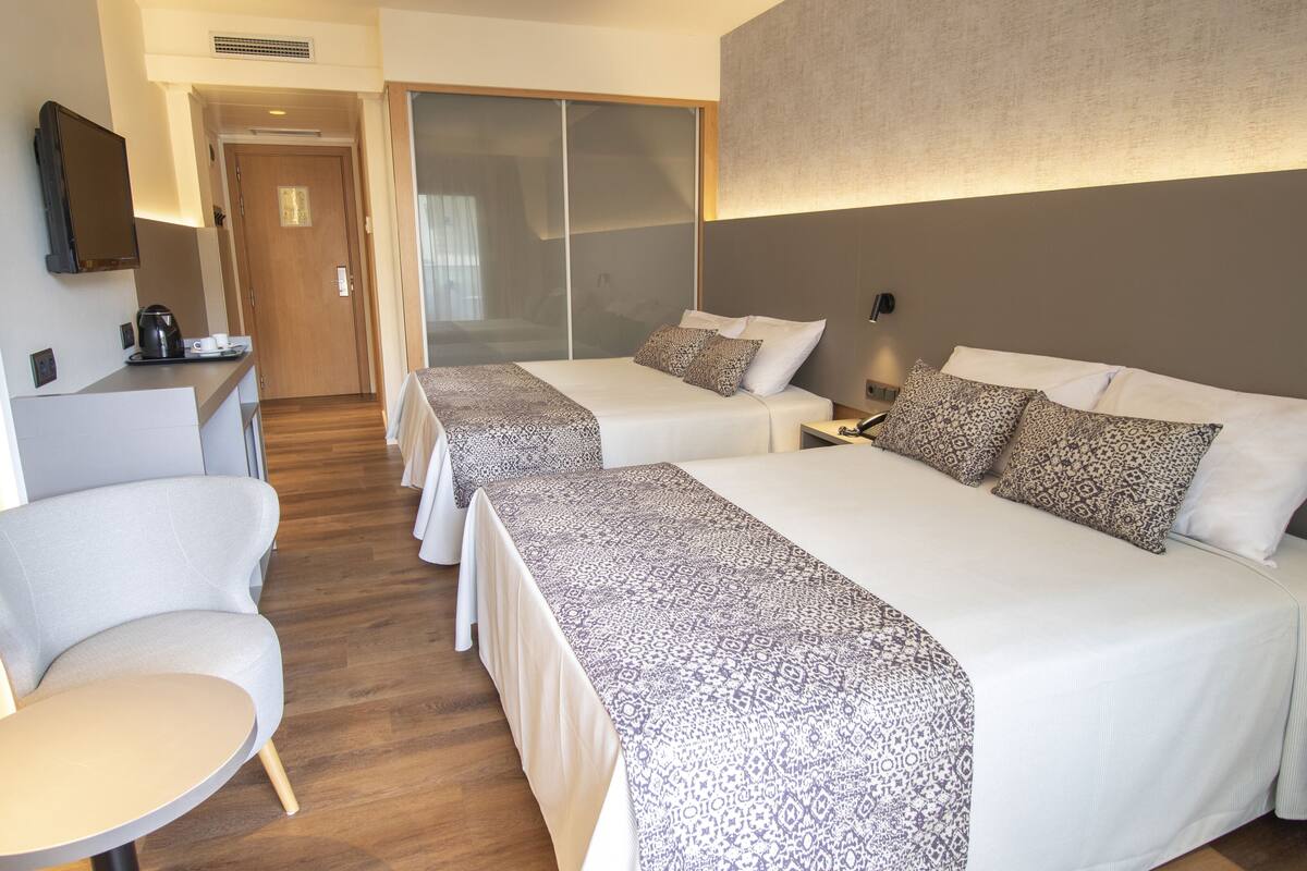 Une chambre d’hôtel avec deux lits, un petit coin salon, une machine à café et une télévision.
