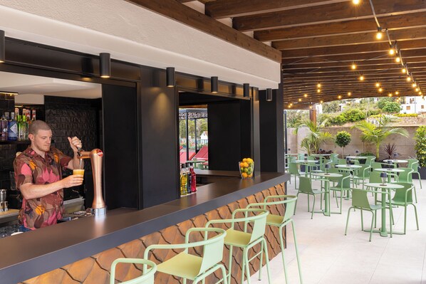 A bar area with a bartender, green chairs, and a stone wall. - Golden Bahía de Tossa & Spa (Tossa de Mar)