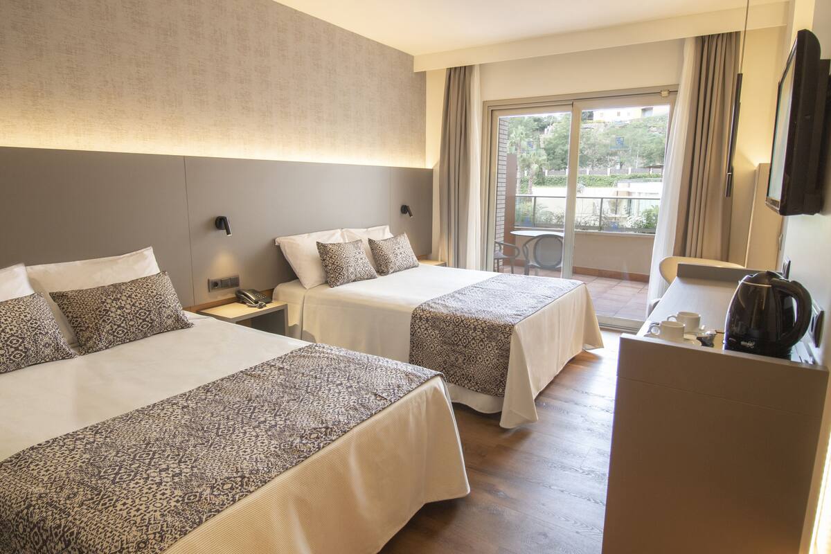 Une chambre d’hôtel avec deux lits, un bureau avec une bouilloire et une vue sur l’extérieur.