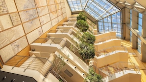 Un atrio de varios niveles con una escalera central, ventanas amplias y una variedad de plantas.
