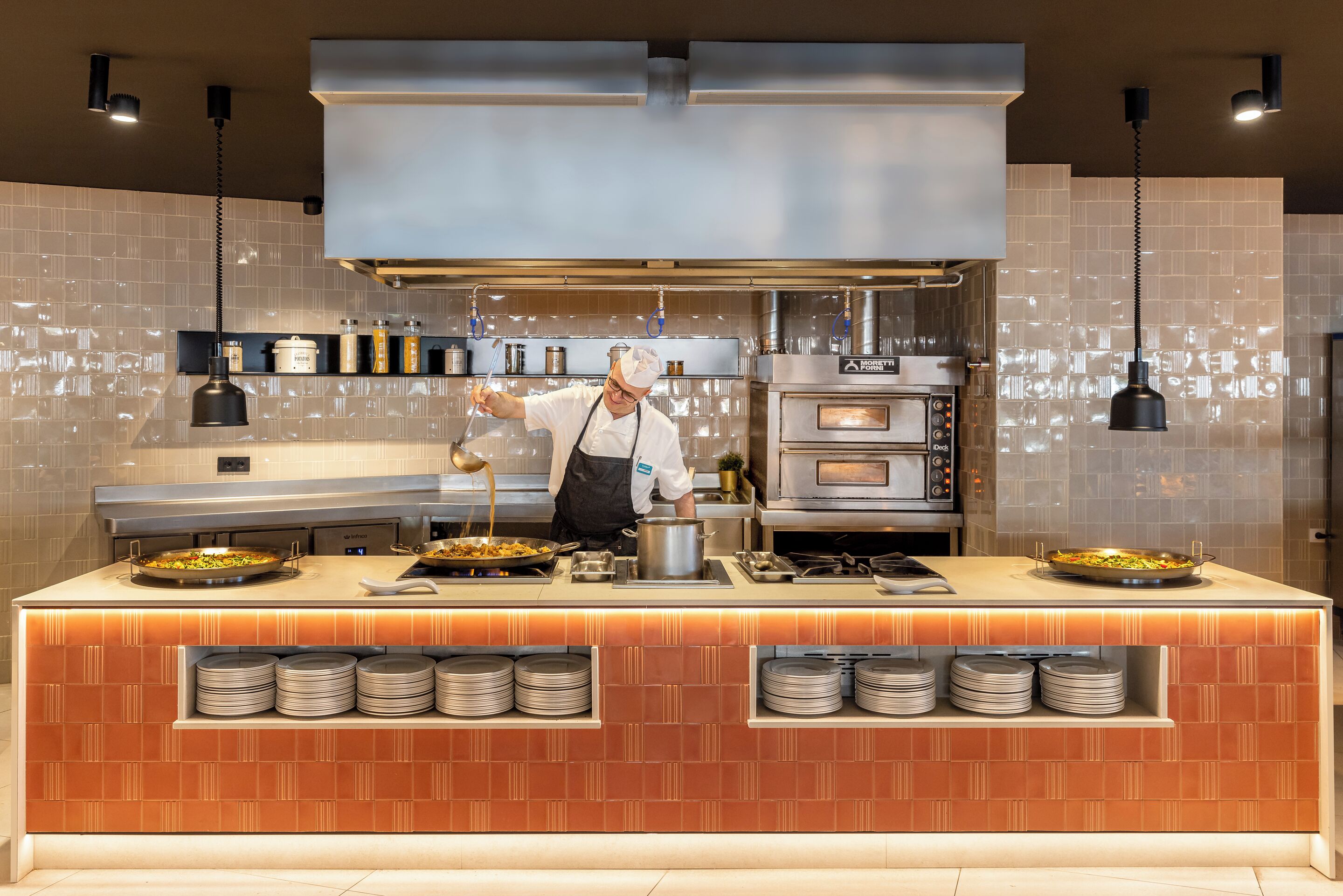 Una cocina moderna con un chef preparando comida, una isla grande con varios platos y hornos empotrados.