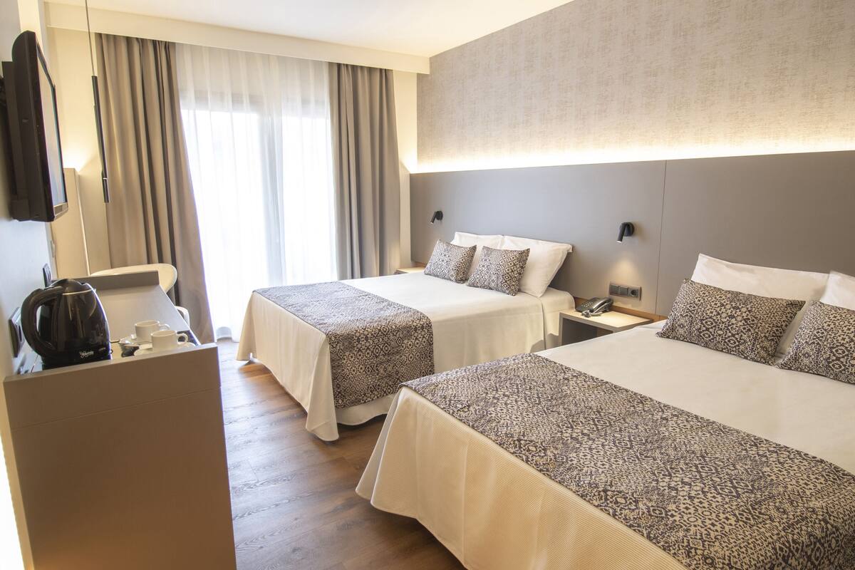 Une chambre d’hôtel avec deux lits, un bureau avec une machine à café, une télévision et une grande fenêtre avec des rideaux.