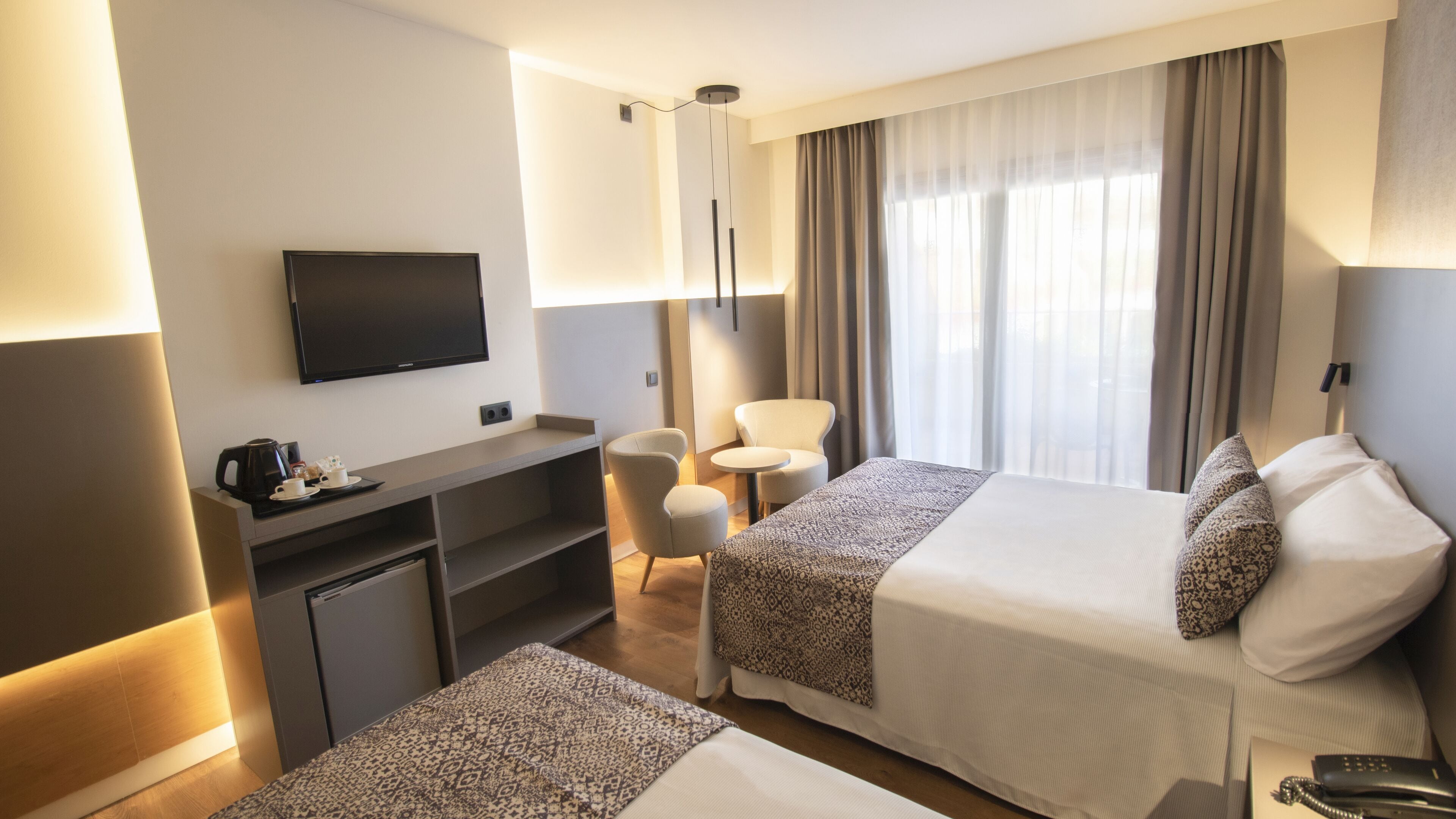 A hotel room with a bed, a desk, a chair, a television, and a window with curtains.