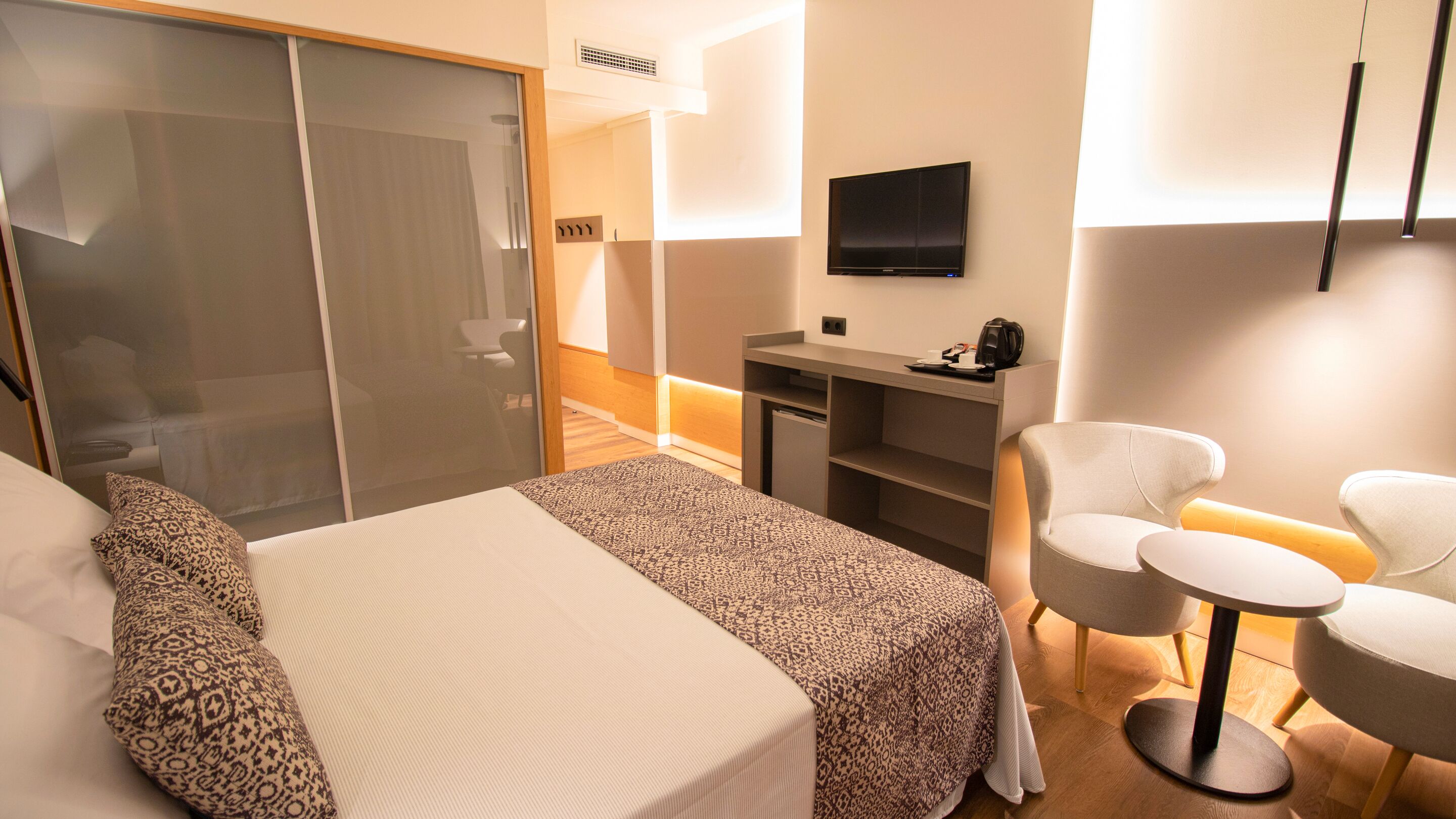 Quarto de hotel com cama, escrivaninha, cadeira e televisão.