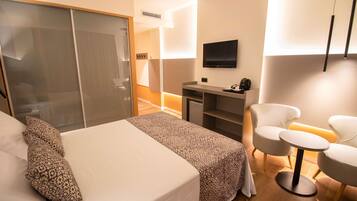 Quarto de hotel com cama, escrivaninha, cadeira e televisão.