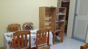 Un coin repas avec une table dressée pour quatre personnes, des chaises en bois, une bibliothèque en bois et une porte visible au fond.