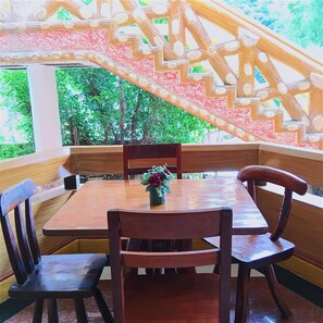 A wooden dining table with four chairs, a vase with flowers, and a staircase with a geometric design. - Big Creek Mansion (El Nido)