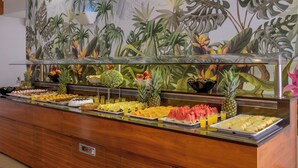 A buffet with tropical-themed wall art, a variety of fruits, and a digital clock. - Eurohotel Katrin Hotel & Bungalows (Hersonissos)