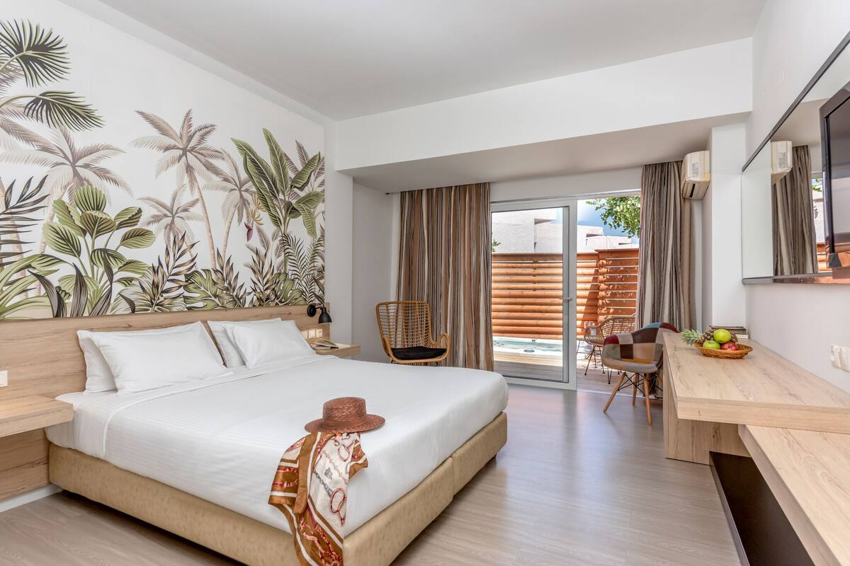 A modern hotel room with a large bed, a desk, and a dining area.