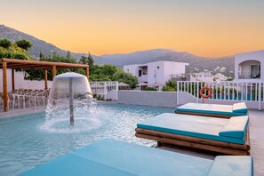 A pool with a water feature, lounge chairs, and a view of buildings and mountains.