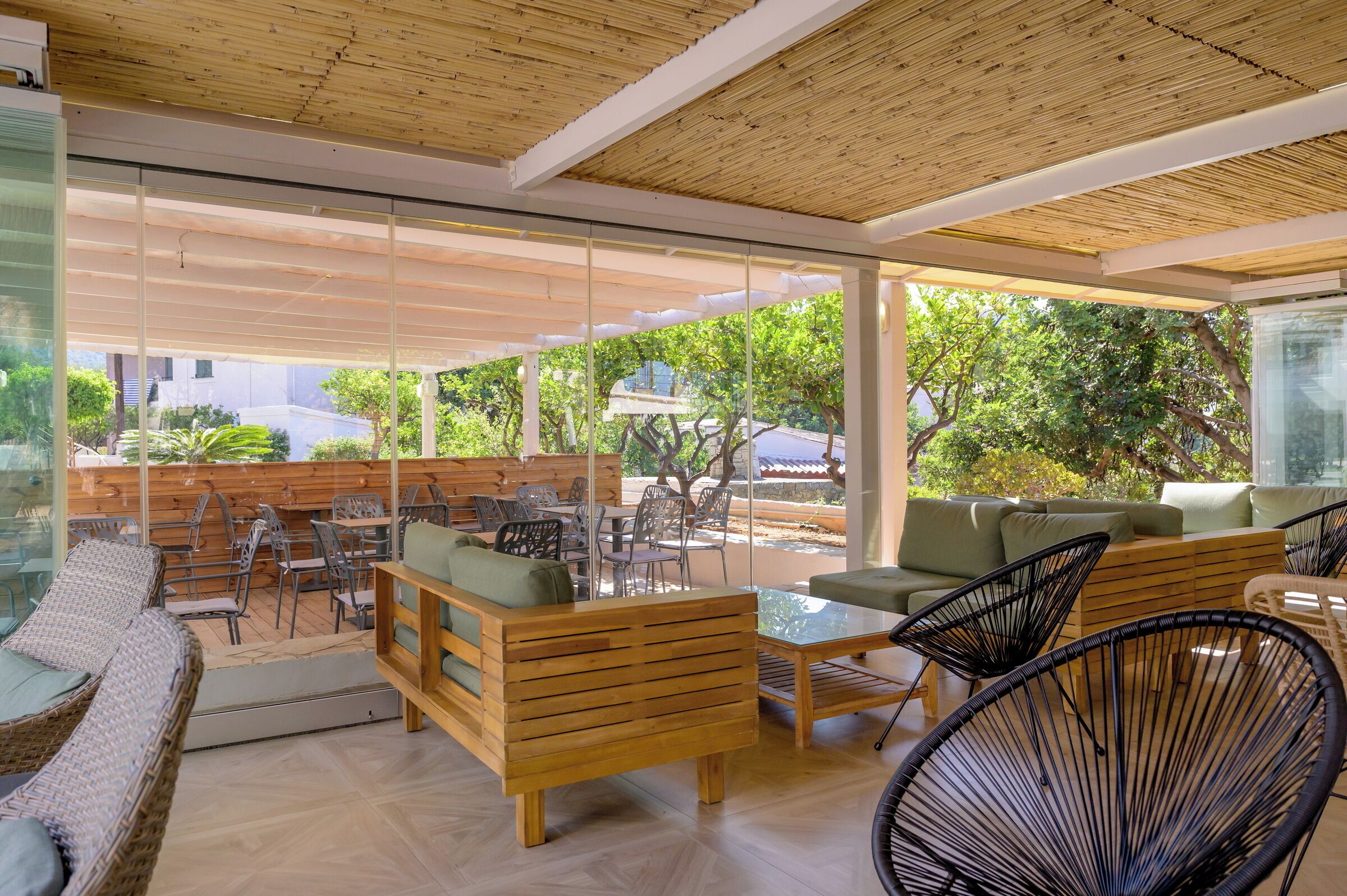 An outdoor seating area with wooden furniture, glass partitions, and a view of greenery.