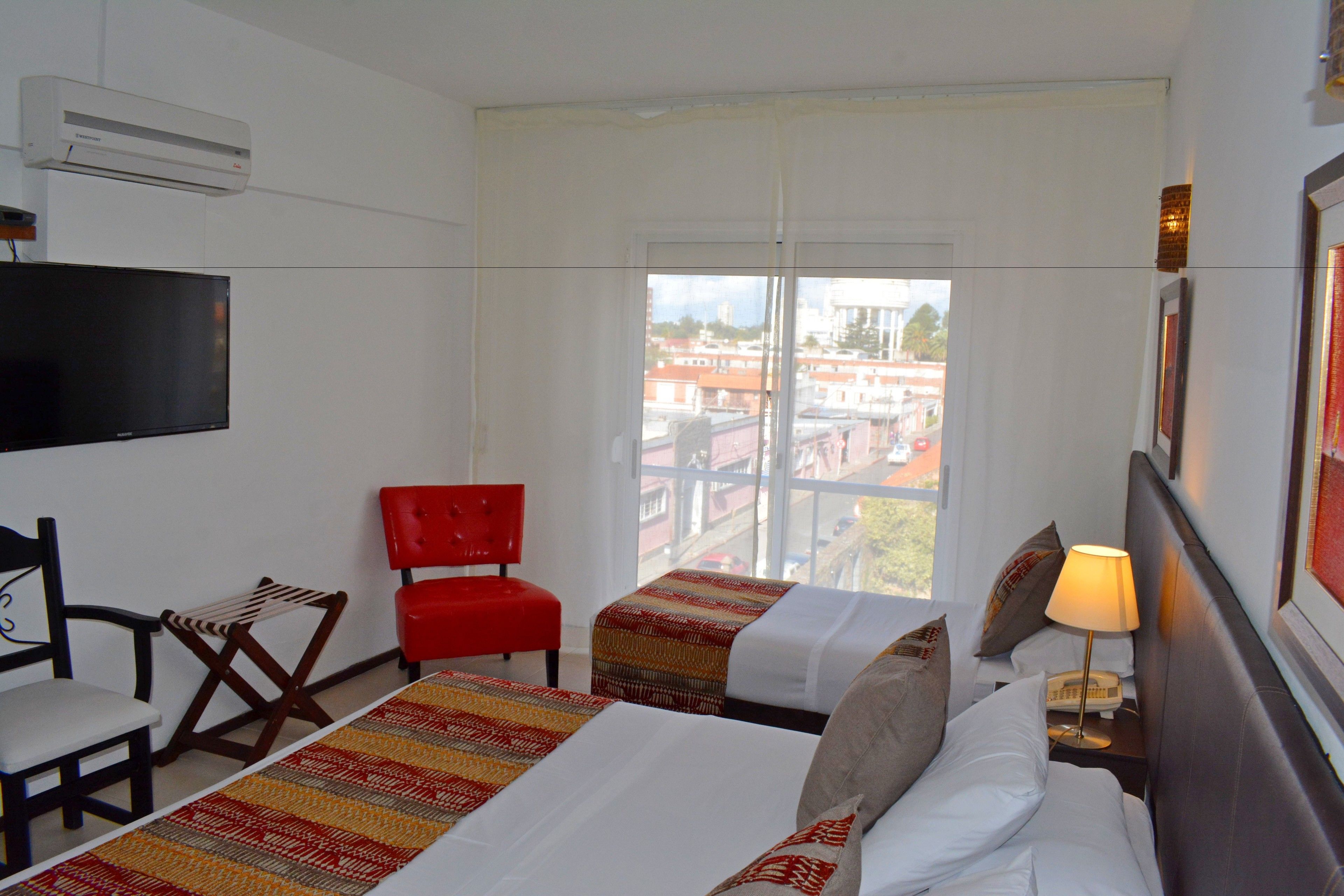 Een hotelkamer met twee bedden, een televisie, een rode stoel en een raam met uitzicht over de stad.
