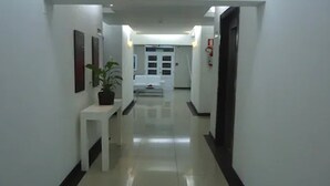 Un pasillo limpio y bien iluminado con un banco blanco, una planta en maceta y un extintor en la pared.
