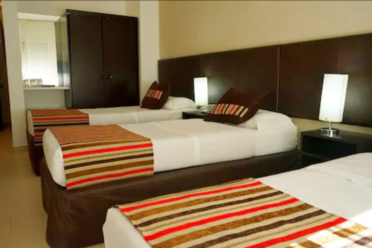 Une chambre d’hôtel avec deux lits, des têtes de lit en bois foncé, du linge de lit blanc, des coussins décoratifs à rayures et des lampes de chevet.