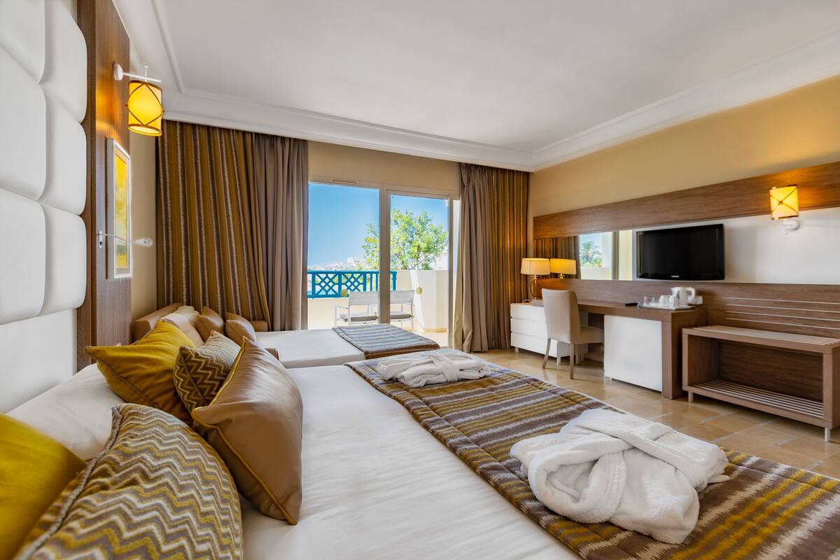 Une chambre d’hôtel avec deux lits, un bureau, une télévision et un balcon avec vue.