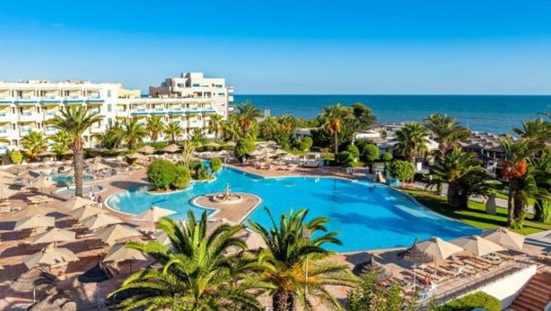 Ein Resort mit einem großen Schwimmbad, Palmen und Blick auf den Ozean.