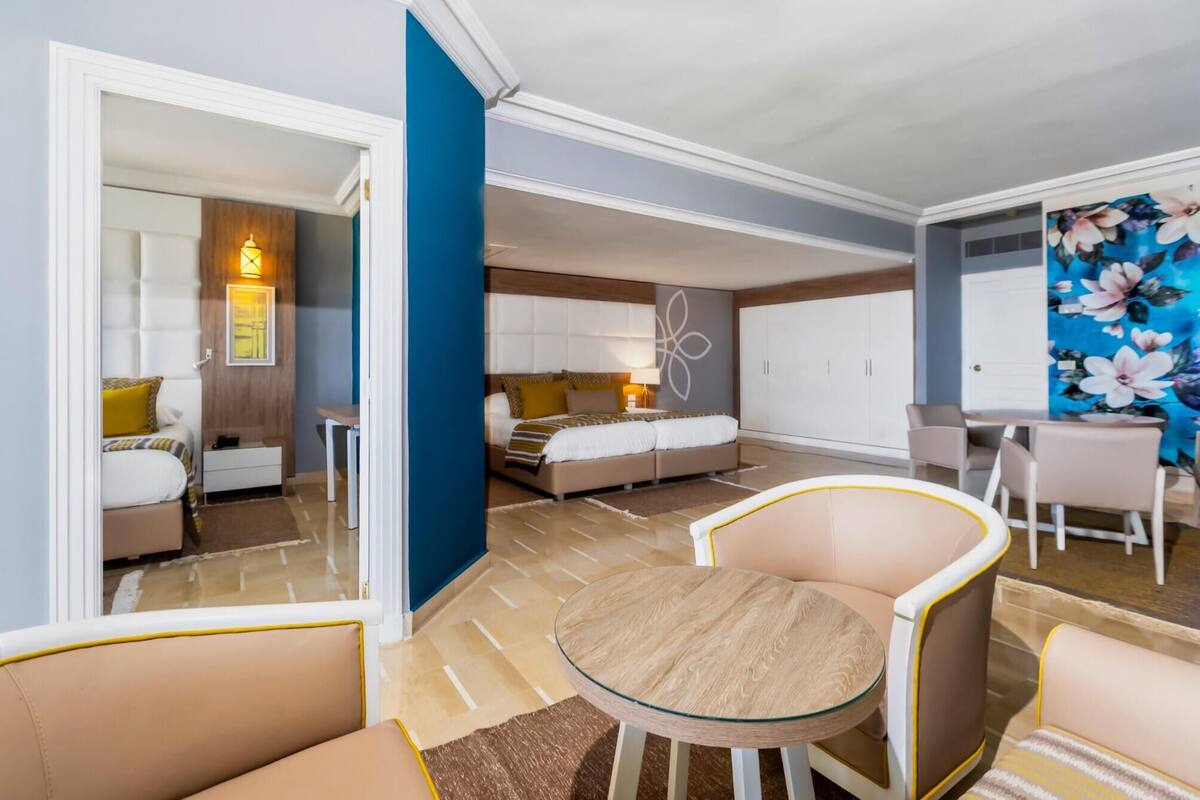 Une chambre d’hôtel moderne comprenant un lit, un coin salon avec une table en verre et un coin repas avec une chaise et une table.