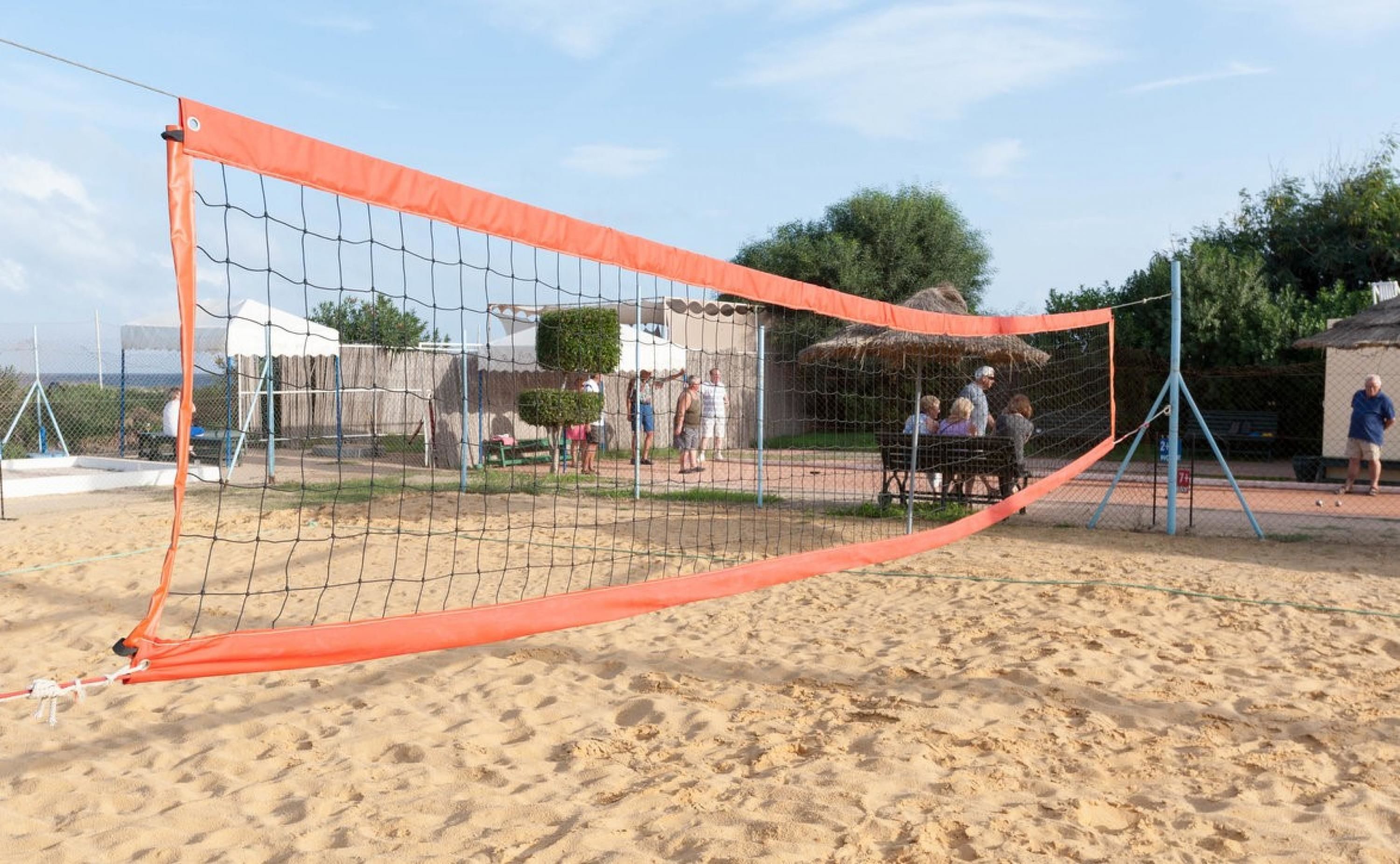 Una rete da pallavolo sulla spiaggia, con persone sullo sfondo.