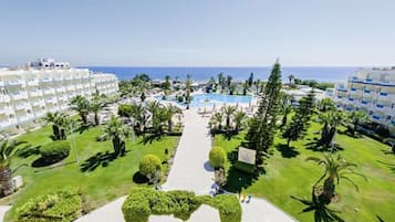 Een resort met een centraal gelegen zwembad, palmbomen en een helder uitzicht op de oceaan.