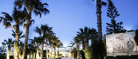 A pathway lined with palm trees and a large mural on the right.