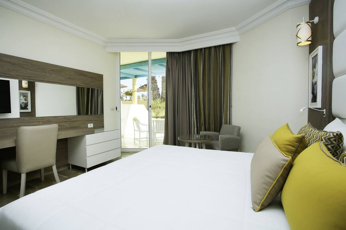 Une chambre d’hôtel avec un grand lit, un bureau, une chaise, une petite table et un balcon avec vue.