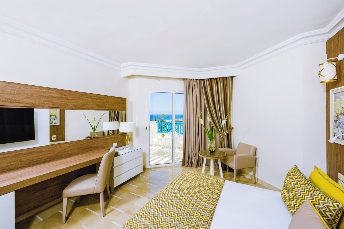Une chambre d’hôtel avec un lit, un bureau, une chaise, une petite table et un balcon avec vue.