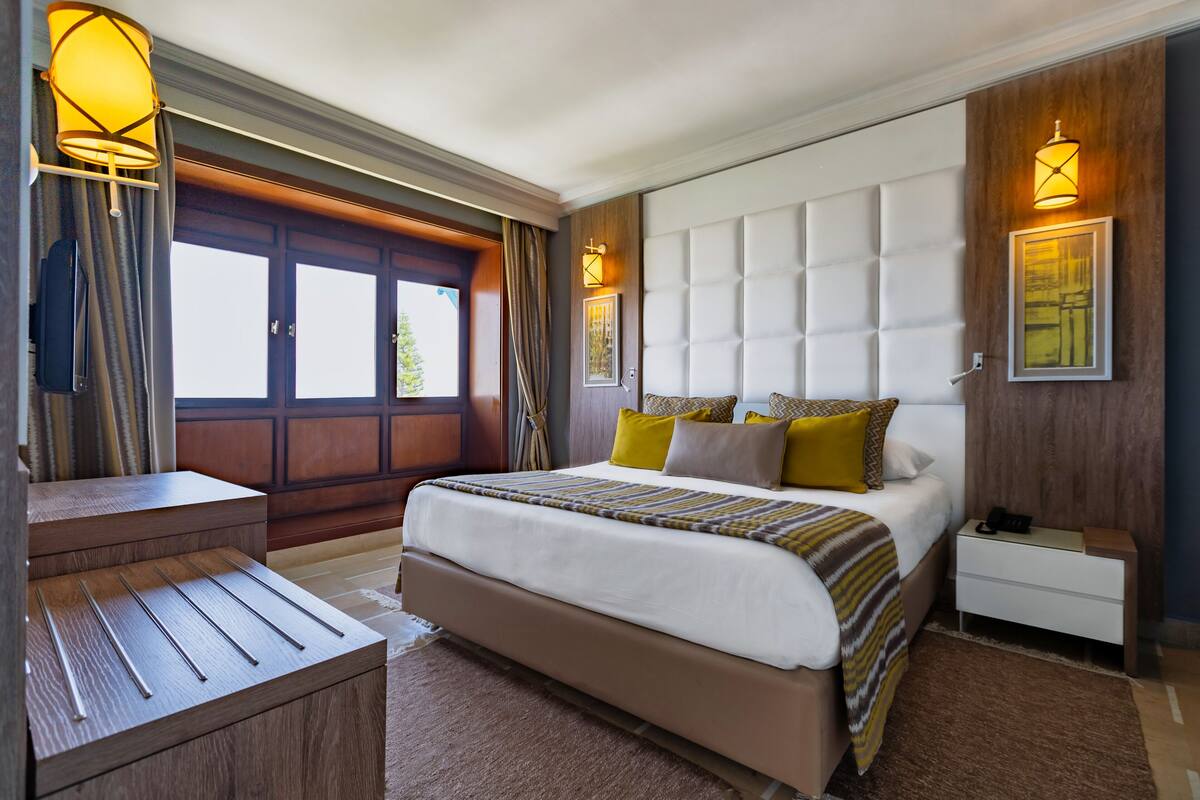 Une chambre moderne avec un grand lit, une table de chevet en bois, un bureau et une fenêtre avec des rideaux.