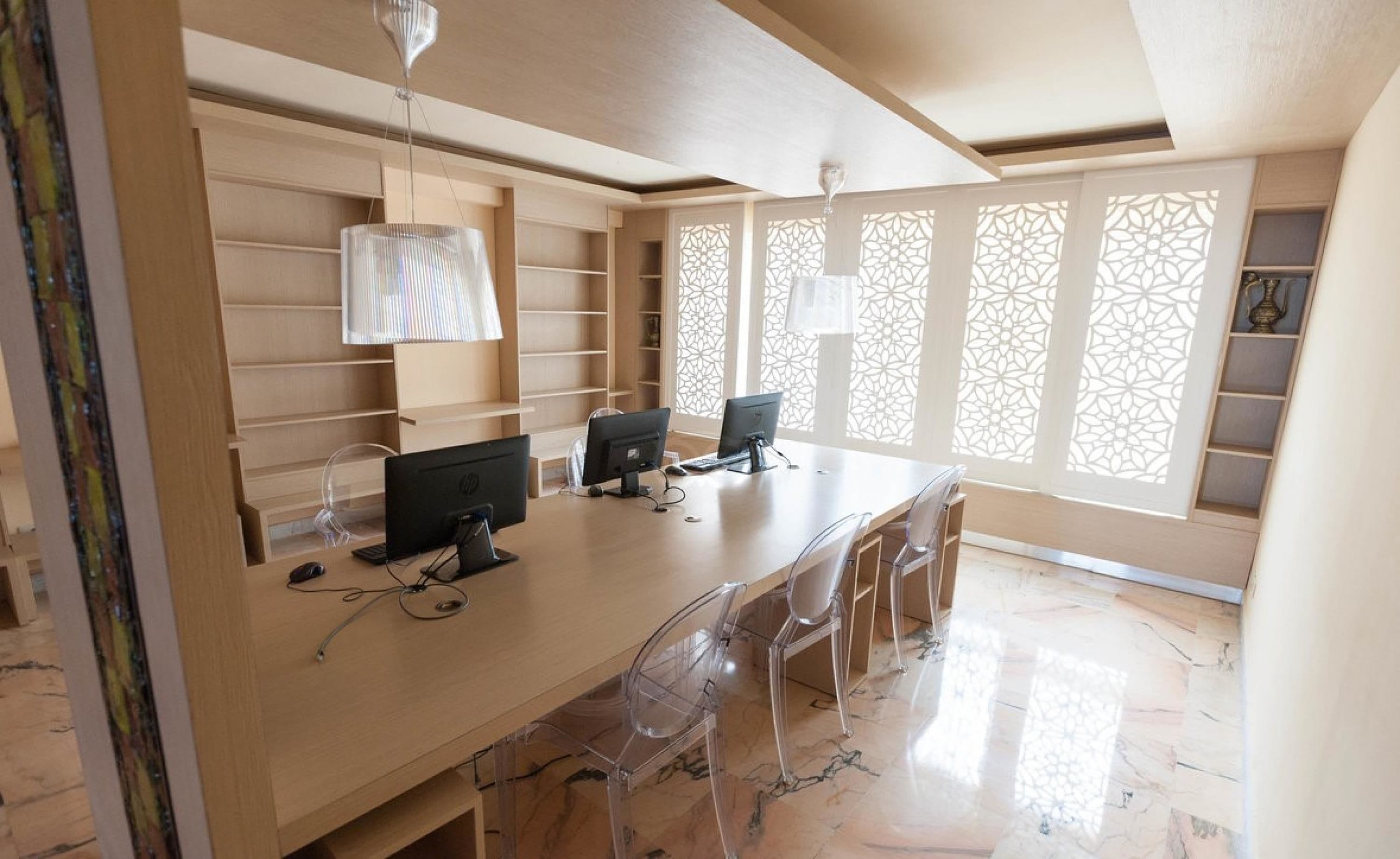 A spacious office with a long table, two computers, and clear plastic chairs.