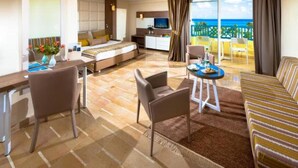 Ein Hotelzimmer mit Bett, Schreibtisch, Stuhl, Sofa und einem Balkon mit Meerblick.