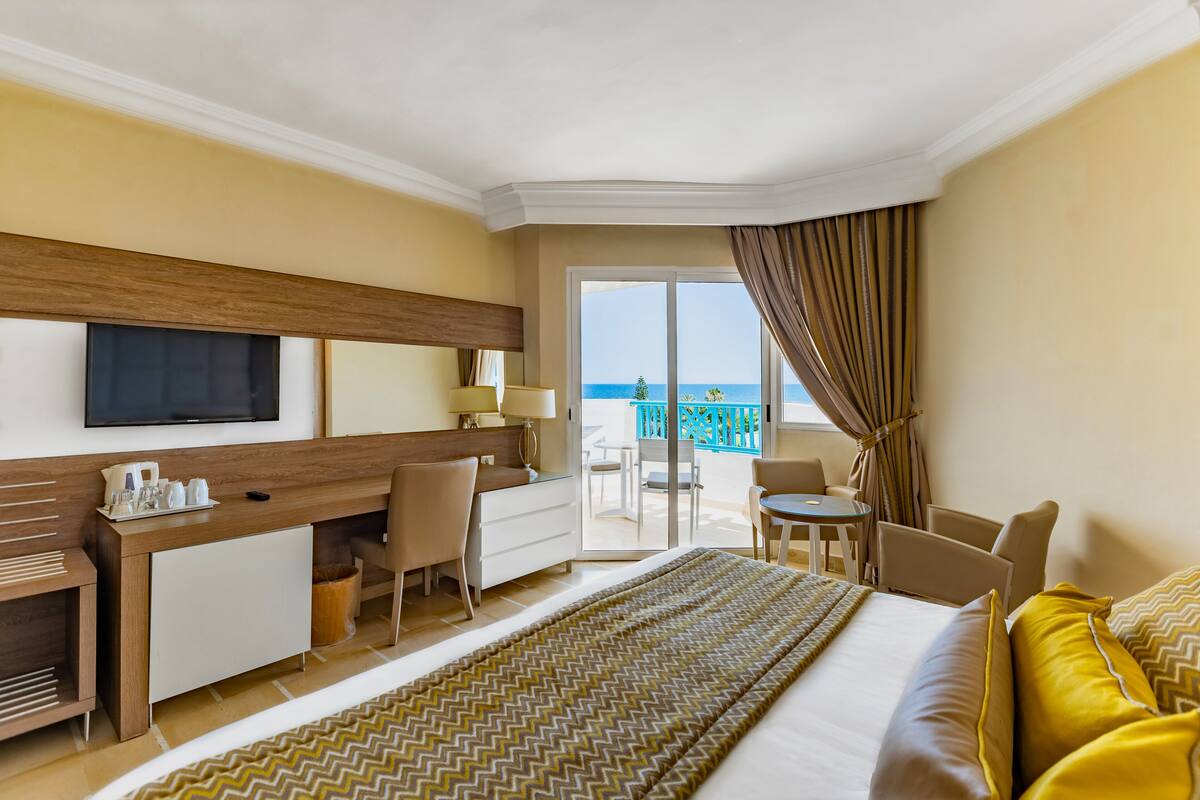 Une chambre d’hôtel équipée d’un lit, d’un bureau, de chaises et d’un balcon avec vue sur la mer.
