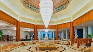 Eine großzügige Lobby mit einer zentralen Sitzecke, einem beeindruckenden Kronleuchter und einer dekorativen Decke.