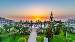 Ein Resort mit Pool, Palmen und Blick auf den Sonnenuntergang über dem Meer.