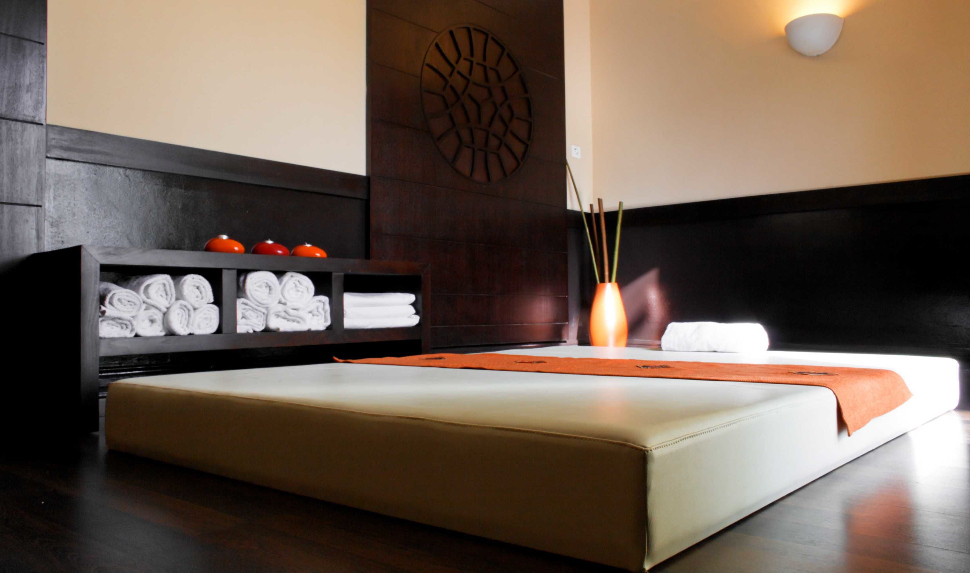 Une chambre d’hôtel moderne avec un grand lit, une tête de lit en bois foncé, une étagère intégrée où sont rangées les serviettes et un élément décoratif mural.